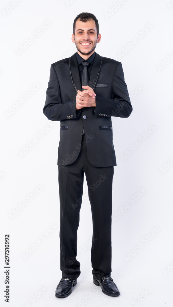 Full body shot of happy young bearded Persian businessman in suit Full body shot of happy young bearded Persian businessman in suit