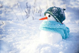 Little cute snowman in a knitted hat and scarf on snow on a sunny winter day. Christmas card