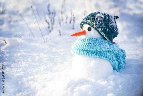 Little cute snowman in a knitted hat and scarf on snow on a sunny winter day. Christmas card © isavira