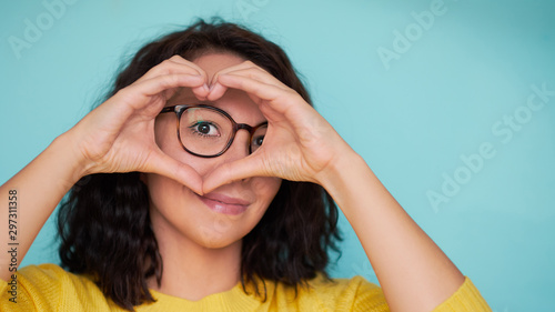 woman in glasses on a turquoise background makes a heart shape with her hands, a symbol of love