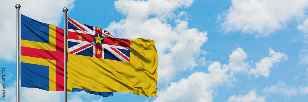 Aland Islands and Niue flag waving in the wind against white cloudy blue sky together. Diplomacy concept, international relations. Aland Islands and Niue flag waving in the wind against white cloudy blue sky together. Diplomacy concept, international relations.