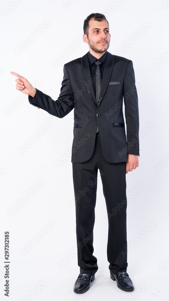 Full body shot of young bearded Persian businessman in suit pointing finger and looking away Full body shot of young bearded Persian businessman in suit pointing finger and looking away