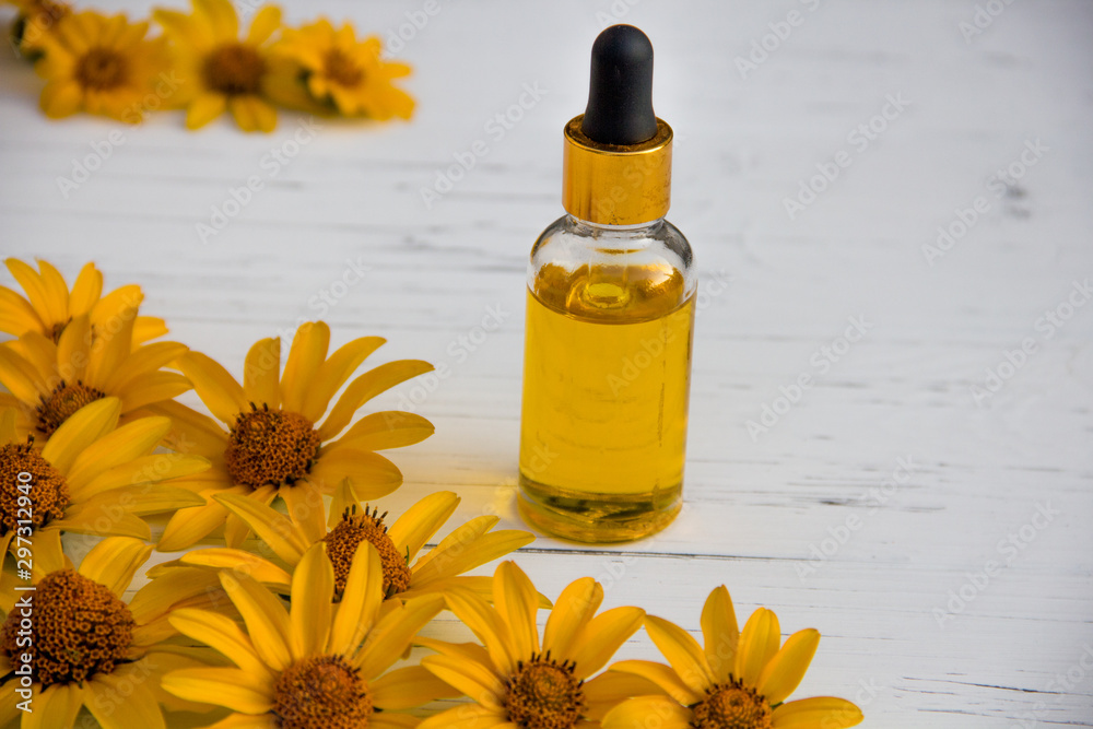 yellow flowers and cosmetic oil in a bottle on a wooden light background yellow flowers and cosmetic oil in a bottle on a wooden light background