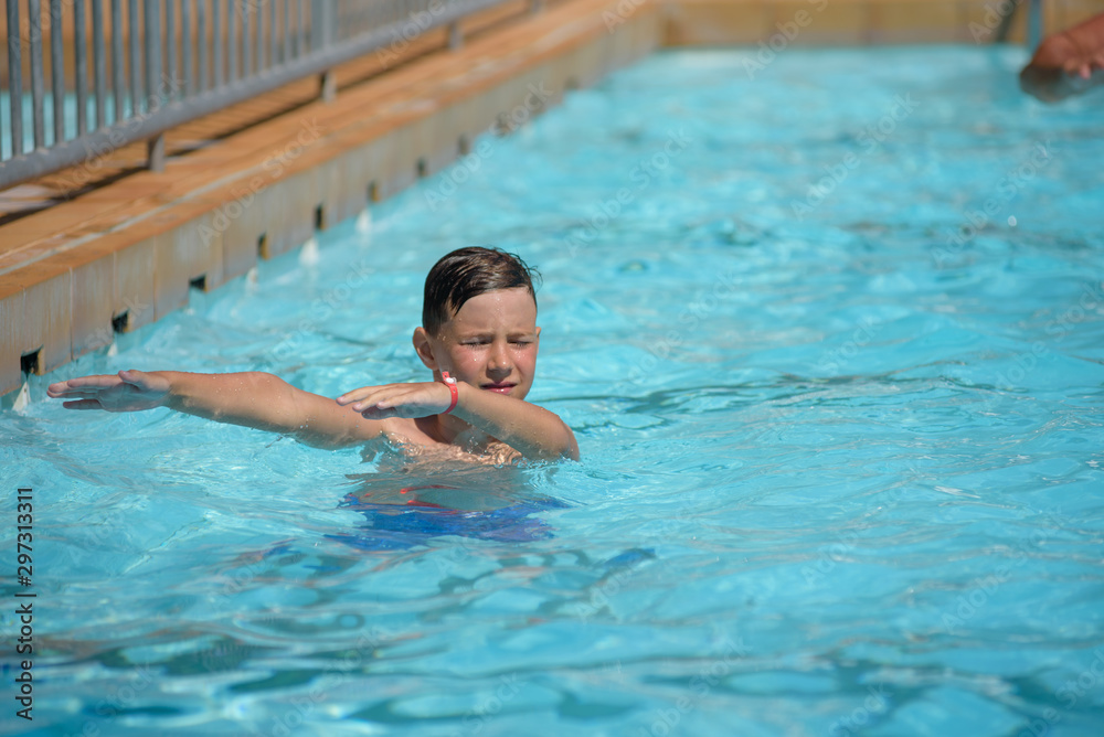 Cute European boy dancing aqua Zumba in hotel’s pool during his summer vacations. Healthy active childhood concept.