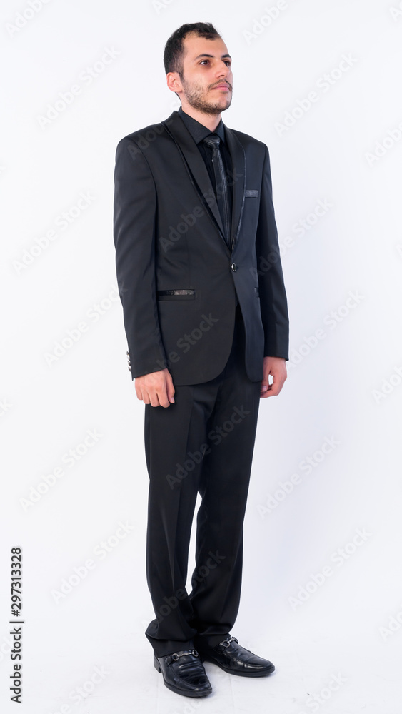 Full body shot of young bearded Persian businessman in suit thinking Full body shot of young bearded Persian businessman in suit thinking