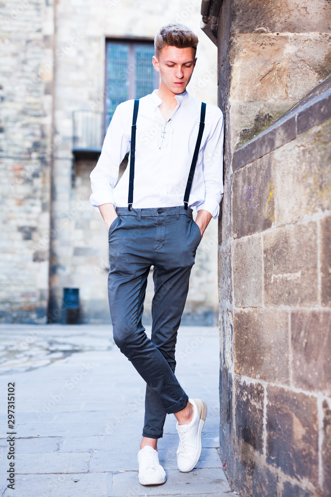 Obraz premium young European guy in shirt and trousers with suspenders walking around city