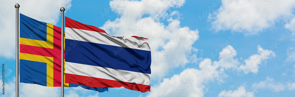 Aland Islands and Thailand flag waving in the wind against white cloudy blue sky together. Diplomacy concept, international relations. Aland Islands and Thailand flag waving in the wind against white cloudy blue sky together. Diplomacy concept, international relations.