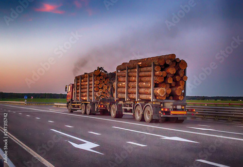 A loaded timber truck transports timber logs with an overload on the highway, black smoke. The concept of transportation of timber and wood, copy space, business