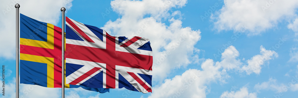 Aland Islands and United Kingdom flag waving in the wind against white cloudy blue sky together. Diplomacy concept, international relations. Aland Islands and United Kingdom flag waving in the wind against white cloudy blue sky together. Diplomacy concept, international relations.