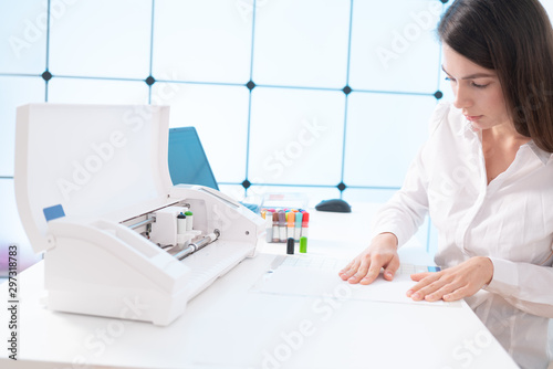 Young woman in printing office insert paper and color pens on plotter