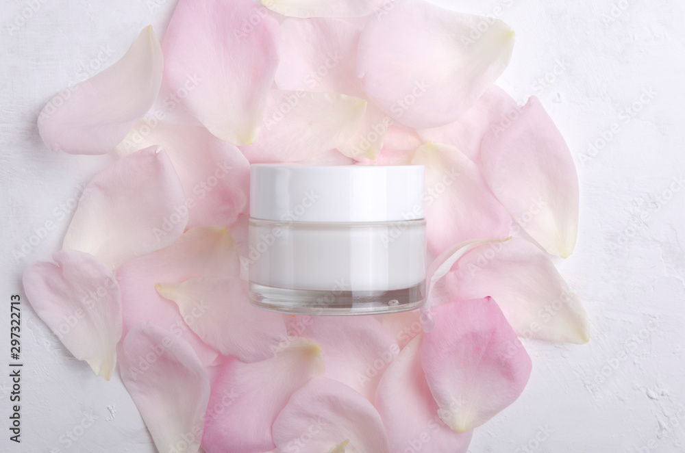 Top view of closed glass jar full of moisturizing cream on the pink rose petals Top view of closed glass jar full of moisturizing cream on the pink rose petals