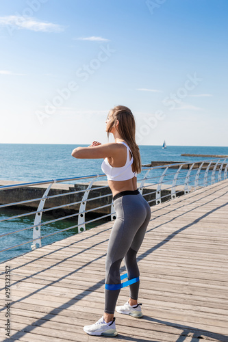 Woman in sportswear squatting with fitness rubber.