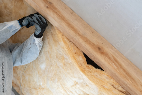 Professional worker man installing thermal insulation layer with fiberglass wool under the roof photo