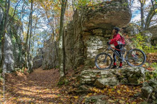 nice senior woman riding her electric mountain bike in the autumnal atmosphere in the Hells Holes of the Swabian Alb near the city of Urach, Baden Wuerttemberg, Germany