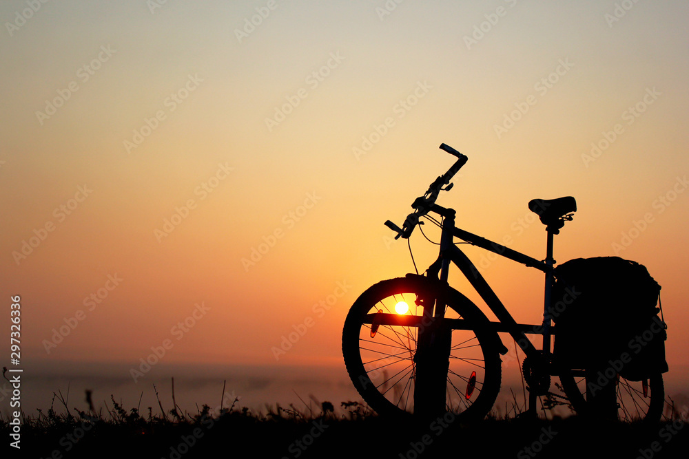 Obraz premium Silhouette of a bicycle against the orange sky at sunrise