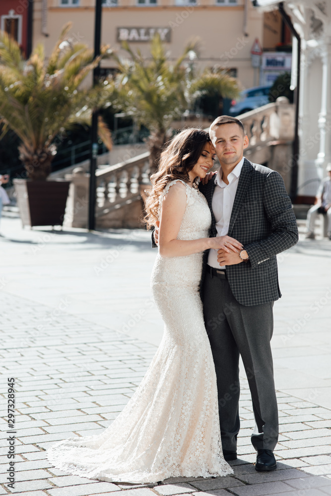 Fototapeta premium Happy couple in love on the background of buildings. Love story of couple in the city. Love story. Portrait of a beautiful young couple in love standing and kissing
