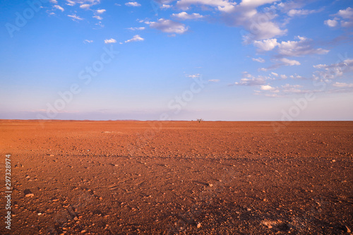 Désert plat et hostile avec une lumière orangée de fin de journée et un ciel bleu et quelques nuages blancs en Namibie - Afrique