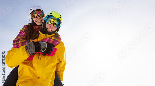 Young happy couple in snowy mountains. Winter sport vacation. activity holiday concept. the girl hugs the guy and they are in ski helmets, masks and bright clothes. clean background and edit space