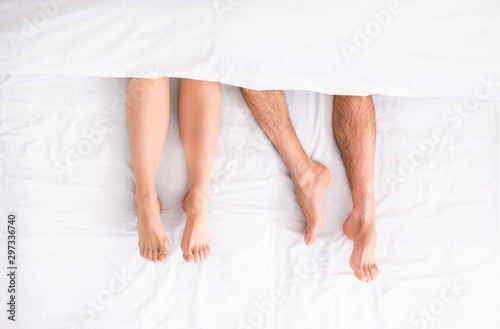 Millennial couple legs under duvet laying on bed