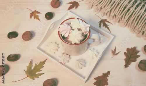 Autumn composition with a cup of meringues, yellow leaves, chestnuts, walnuts and wool blanket on a white wooden background