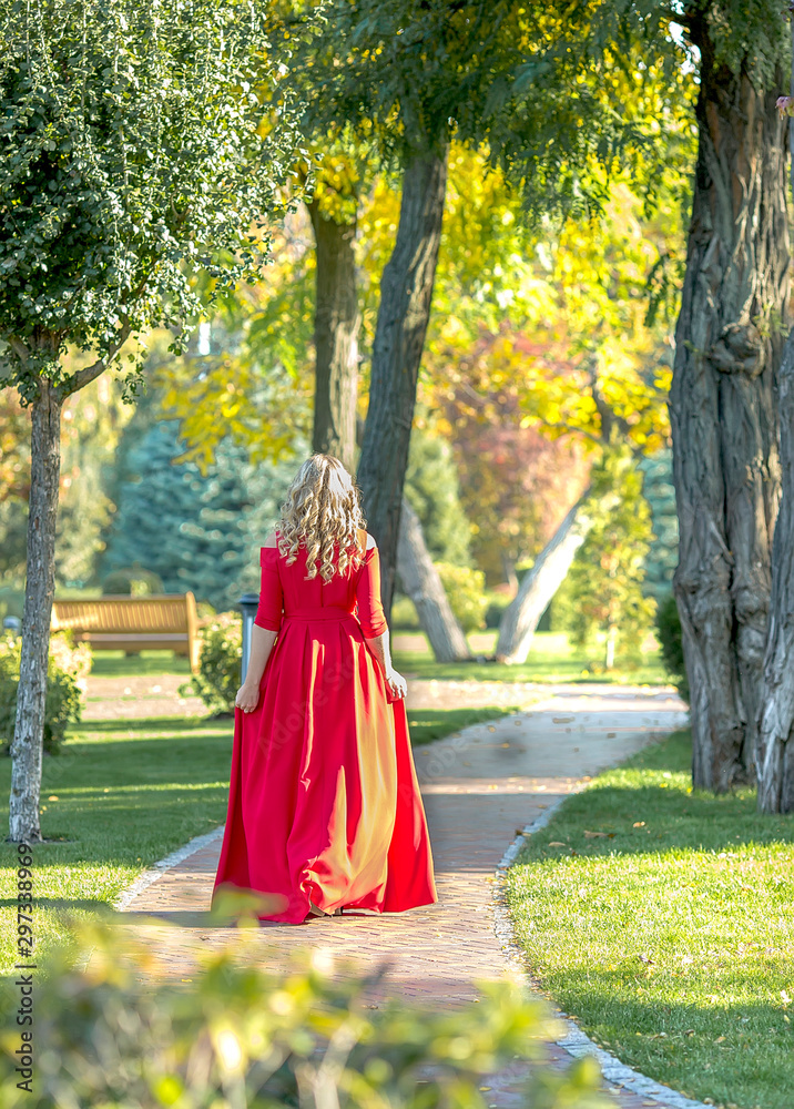 beautiful young woman in a chic red dress walks in the autumn park
