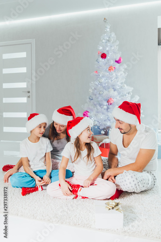 Happy parents and children exchanging gifts near Christmas tree at home