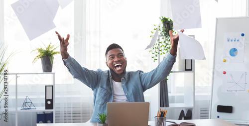 Cheerful african american employee celebrating success throwing papers in office photo