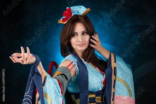 Beautiful smiling leggy busty cosplay girl wearing a stylized Japanese kimono costume cheerfully posing on a blue background. photo