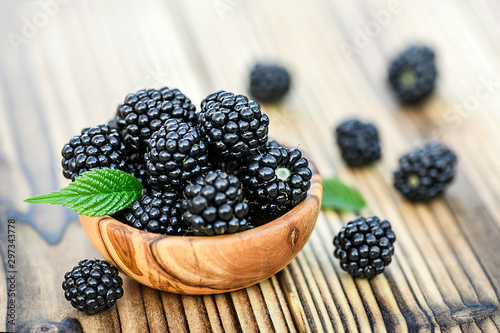 Ripe blackberries in wooden olive bowl on rustic table. Forest fruits and leaves.