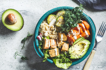 Buddha bowl with quinoa, tofu, avocado, sweet potato, brussels sprouts and tahini dressing, top view. Healthy vegan food concept.