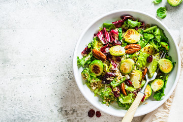 Fried brussels sprouts salad with quinoa, cranberries and nuts in white bowl, top view. Healthy vegan food concept.