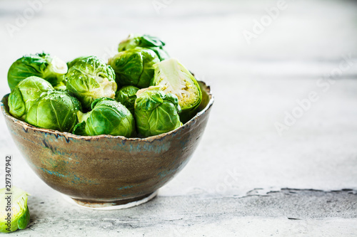 Raw brussels sprouts in bowl, gray concrete background. Healthy vegan food concept.