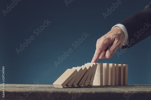 Business crisis manager stopping collapsing dominos with his finger
