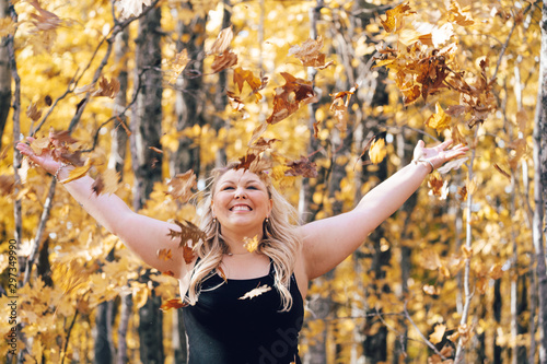 Young attractive blonde woman throiwng autumn leaves in the air, in the forest, full of fall colors. Concept for autumn and fall seasons photo