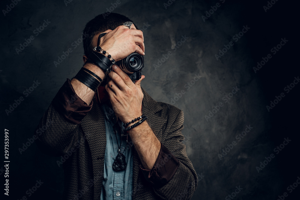 Focused young photographer is taking a photo on the dark grunge background.