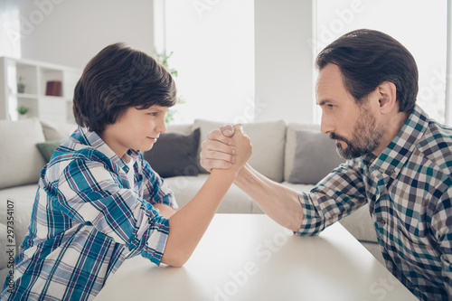 Close-up profile side view portrait of two nice attractive lovely focused concentrated serious guys dad and pre-teen son arm wrestling in light white modern style interior house living-room