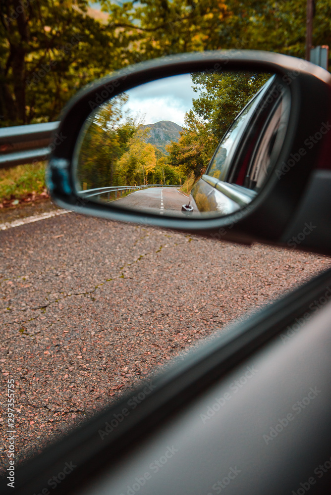 VVertical view of a mountain peak and  forest in autumn from the rearview mirror of a car on the road. 