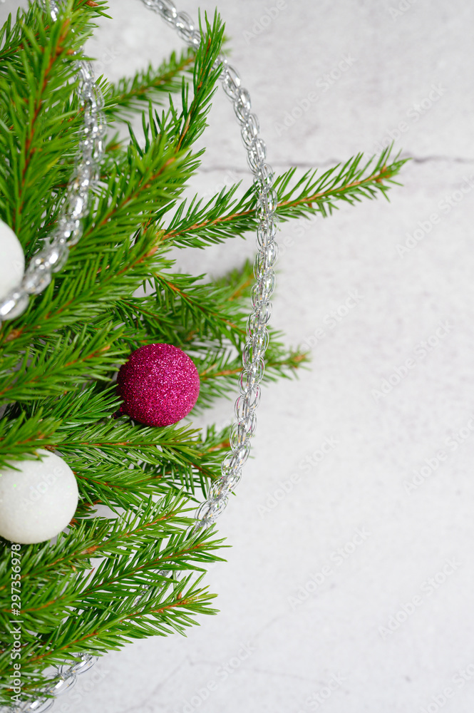 fragment of a christmas tree or fir branches decorated with christmas decorations toys balls, on the background of a white concrete wall. 