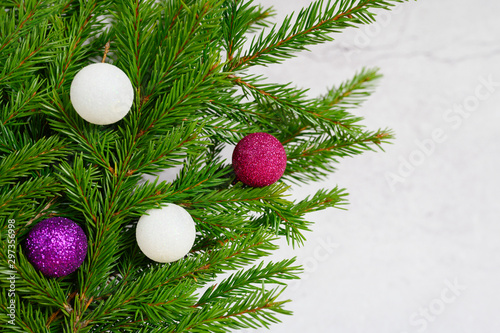 fragment of a christmas tree or fir branches decorated with christmas decorations toys balls  on the background of a white concrete wall