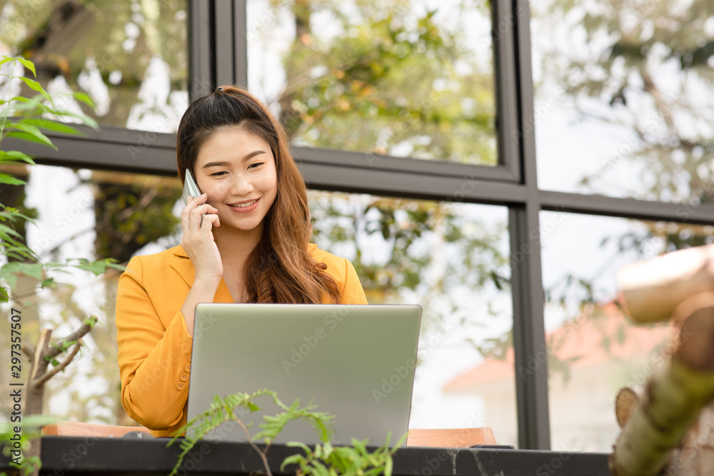 Fototapeta premium Business Asian young woman working with laptop smile and talking with customer in smartphone to get idea and requirement for success job outside office in coffee shop,Small Business Startup Concept