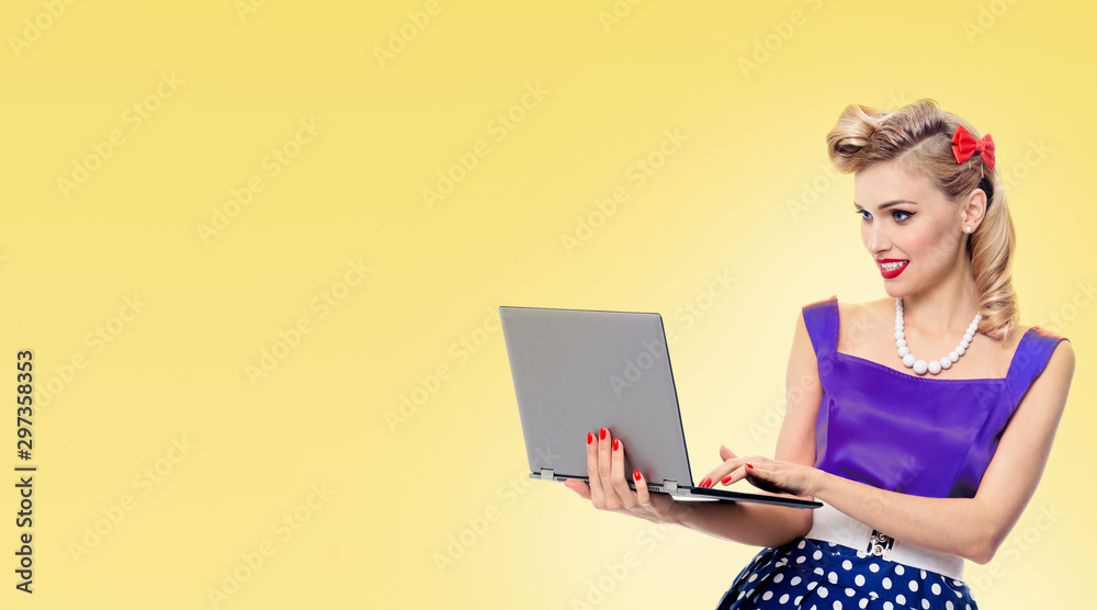 Portrait of beautiful woman using notebook computer, in pin-up style dress in polka dot, with copy space for some slogan or advertising text message, over yellow background Portrait of beautiful woman using notebook computer, in pin-up style dress in polka dot, with copy space for some slogan or advertising text message, over yellow background