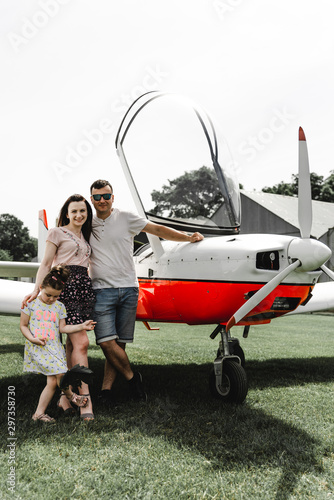 Happy family having fun on the green grass near airplane. Beautiful couple with little daughter posing on the aircraft. Walk at airport