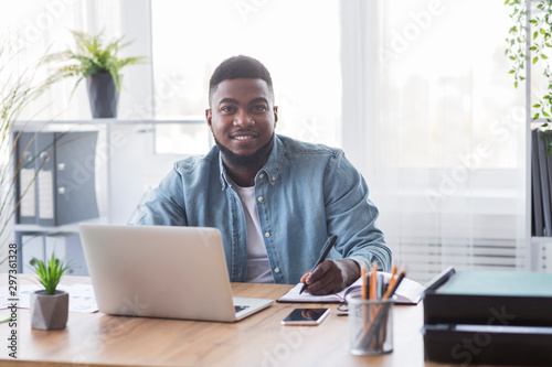 Portrait of smiling black trainee taking notes at new workplace photo