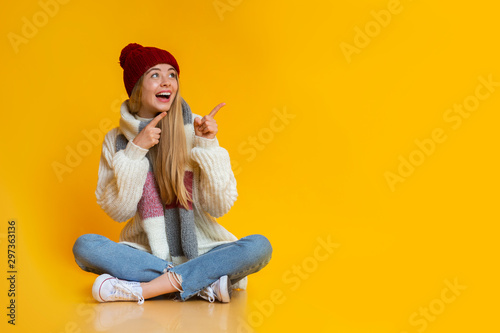 Cheerful woman sitting on floor and pointing at free space © Prostock-studio