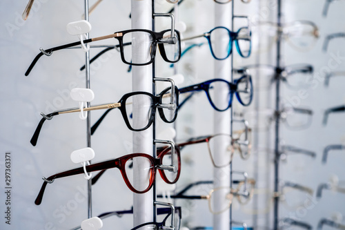 Row of glasses at an opticians. Eyeglasses shop. Stand with glasses in the store of optics. Woman's hand chooses spectacles. Eyesight correction. © Vadim