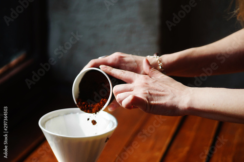 Fototapete Closeup of female barista hands neatly pouring ground coffee into filter for preparing espresso on wooden table
