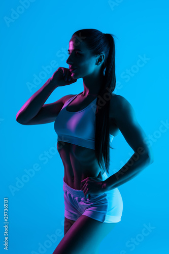 Young sportswoman with perfect body isolated on blue light background
