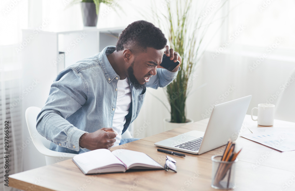 Angry businessman talking on phone and looking at laptop screen Angry businessman talking on phone and looking at laptop screen