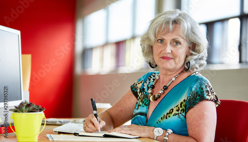 Confident female designer working at her desk in red creative of © AYAimages