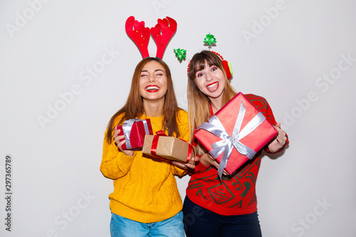 Portrait of two cheery girls dressed in sweaters and christmas hats hugging and looking at camera isolated over white background. Brightfull expressions of happy emotions of two amazing girls friends photo